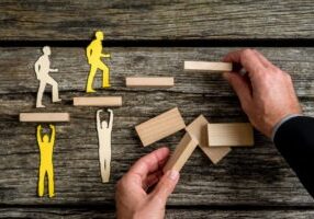 Businessman with silhouette people helping others of opposite color climbing wooden stairs.